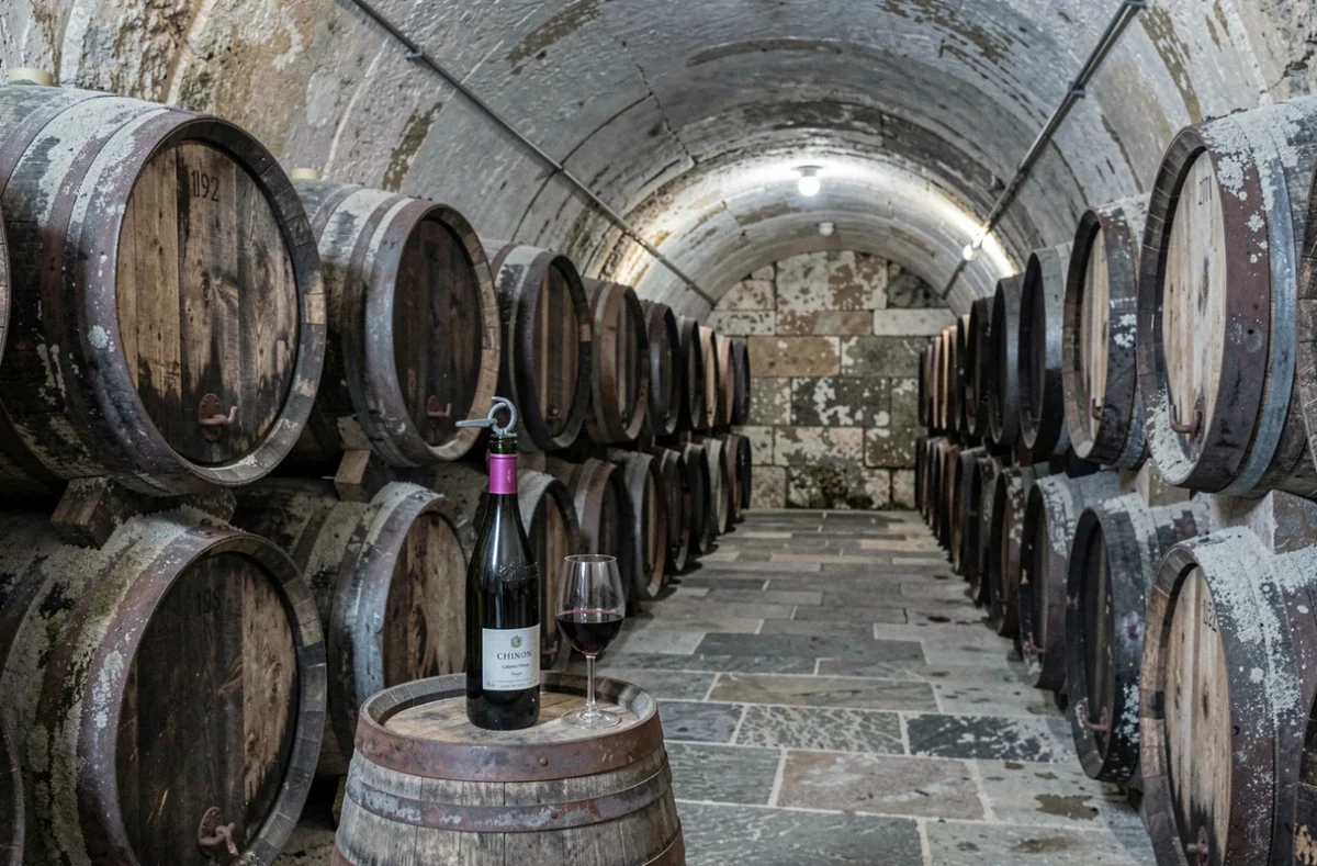 Cave tuffeau en Chinon avec fûts de chêne et verre de Cabernet Franc rubis